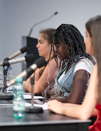 Foto von jungen Frauen, die in Mikrofone sprechen.