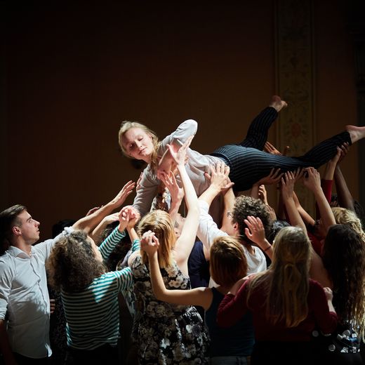 Theatergruppe mit einer Person, die auf Händen getragen wird.