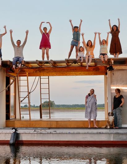 Viele Menschen stehen auf eine Theater-Floß und reißen fröhlich die Hände in die Höhe