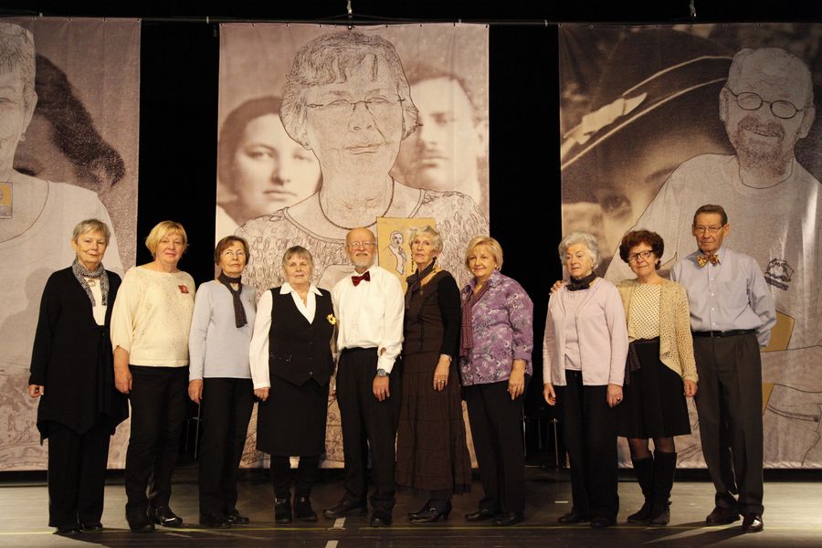 Gruppe älterer Menschen auf Bühne vor Collagen