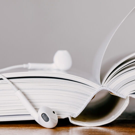 Foto von einem aufgeschlagenen Buch mit Kopfhörern darauf