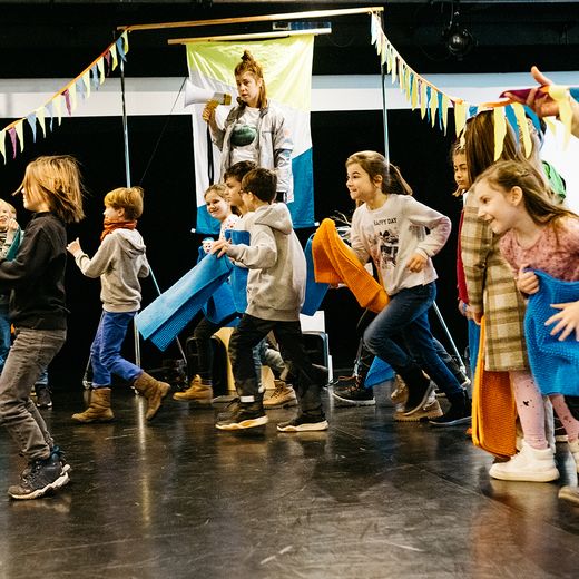 Foto von Kindern mit Handtüchern und einer Frau, die in ein Megafon spricht.