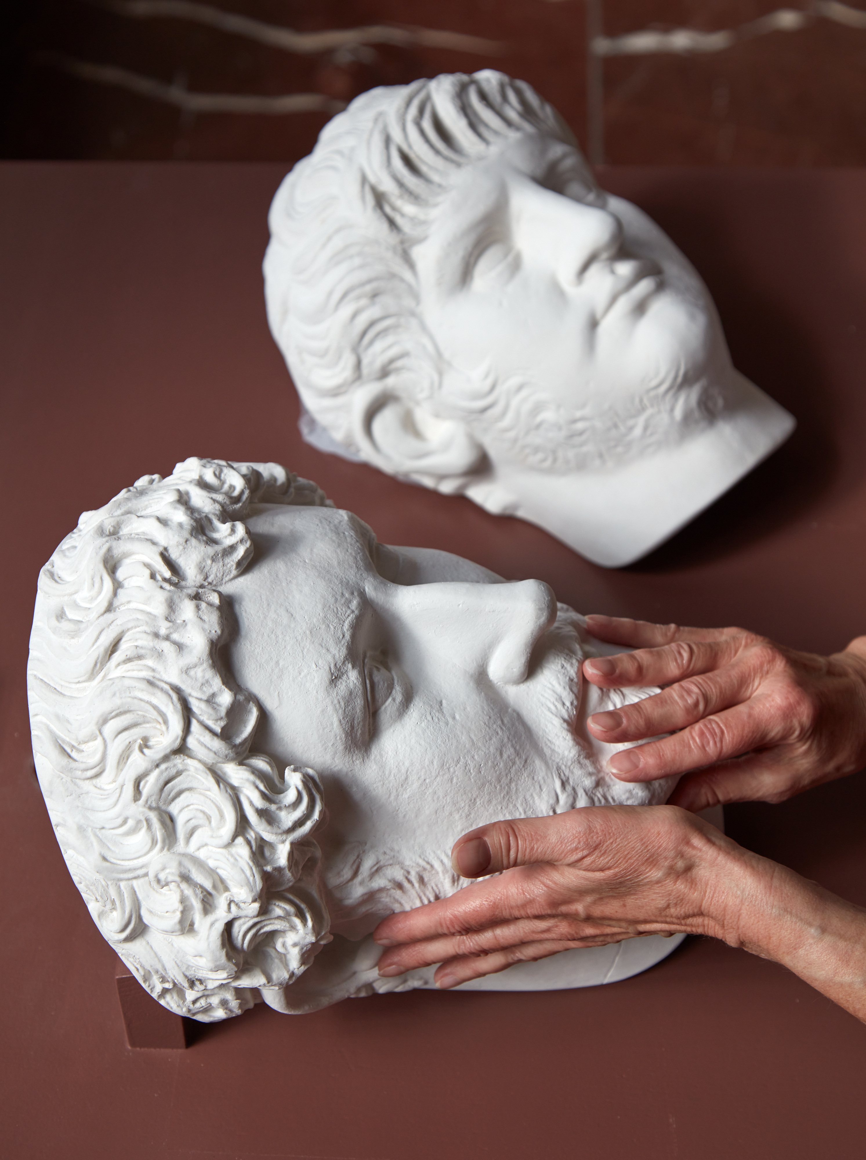 Foto von zwei Büsten. Eine Büste wird von Händen umformt.