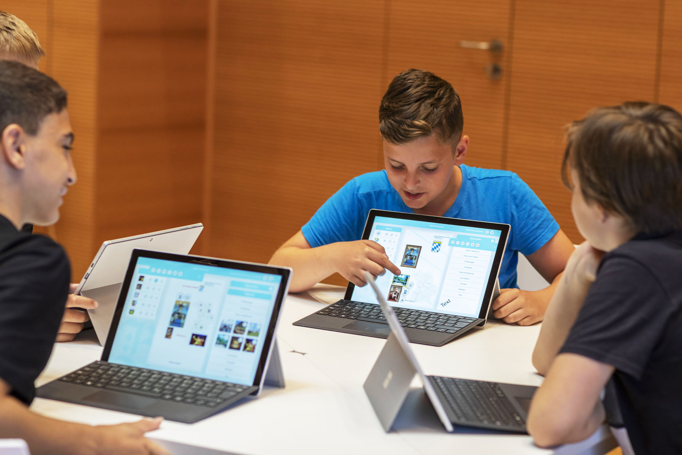 Mehrere Jungen sitzen vor Laptops. Einer zeigt den anderen etwa darauf.