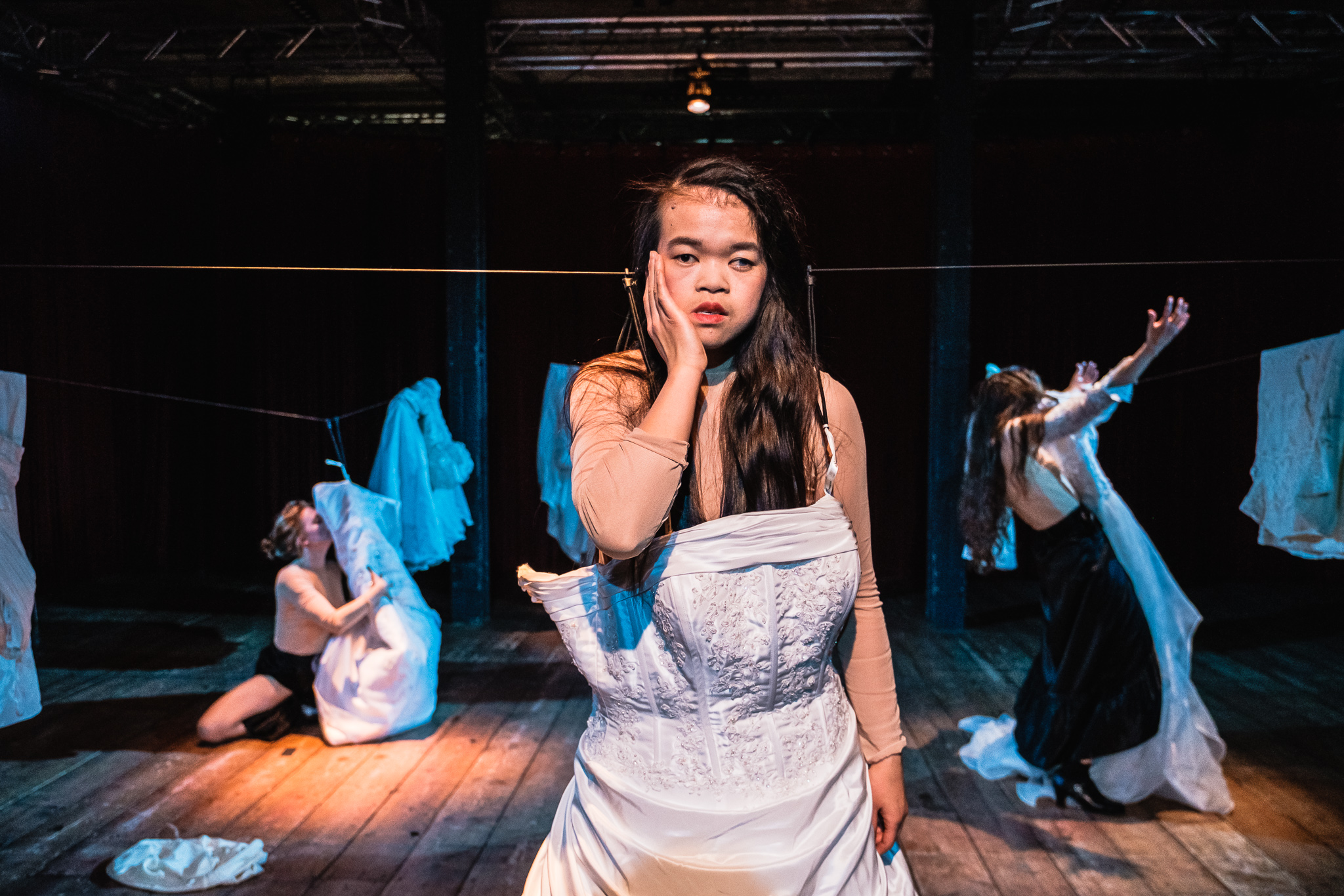 Eine Frau im weißen Kleid singt auf der Bühne. Im Hintergrund sind noch mehr Menschen zu sehen