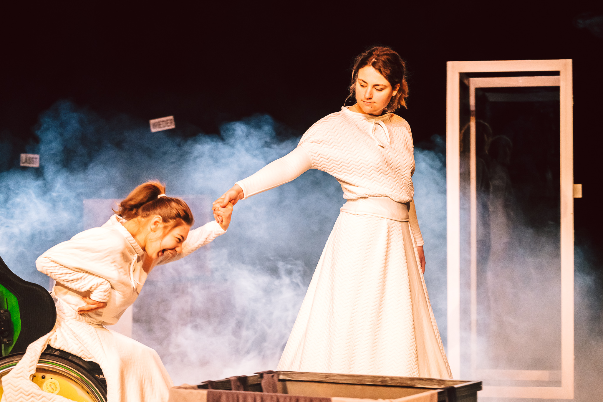 Zwei Frauen in weißen Kleidern auf der Bühne, eine im Rollstuhl, die andere steht